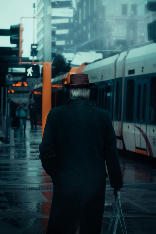 an elderly man walking in the rain on the sidewalk near a train