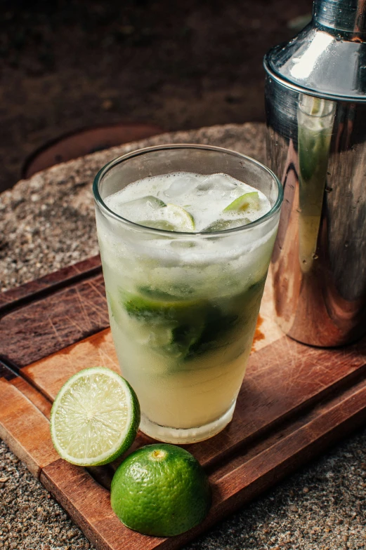 two limes are on a wooden tray next to a glass of water