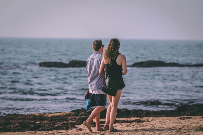 two people standing on a beach facing the ocean