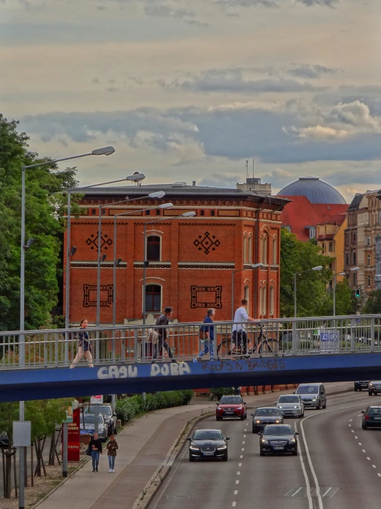 several cars and a bicycle drive on the road while people walk across a bridge