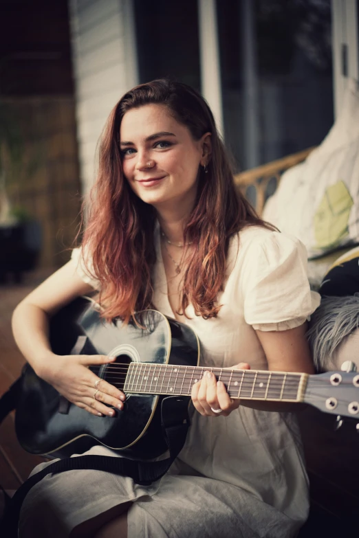 a young woman plays the guitar outside of her home