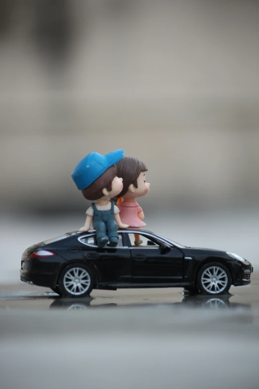 small figurine of boy and girl sitting on top of car