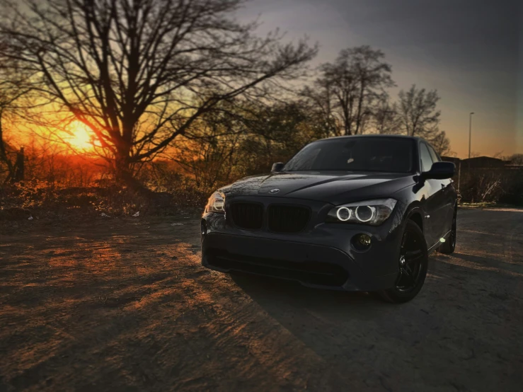 the front end of a black car with a sun setting behind it