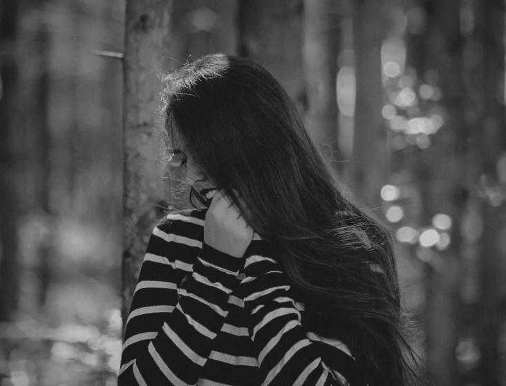 a woman standing in a woods alone with her hair blowing back