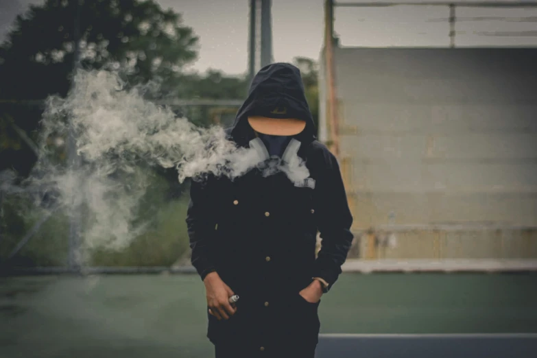 a person in a hoodie standing and smoking a cigarette