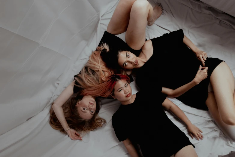 three young women laying on a bed one is wearing a black dress