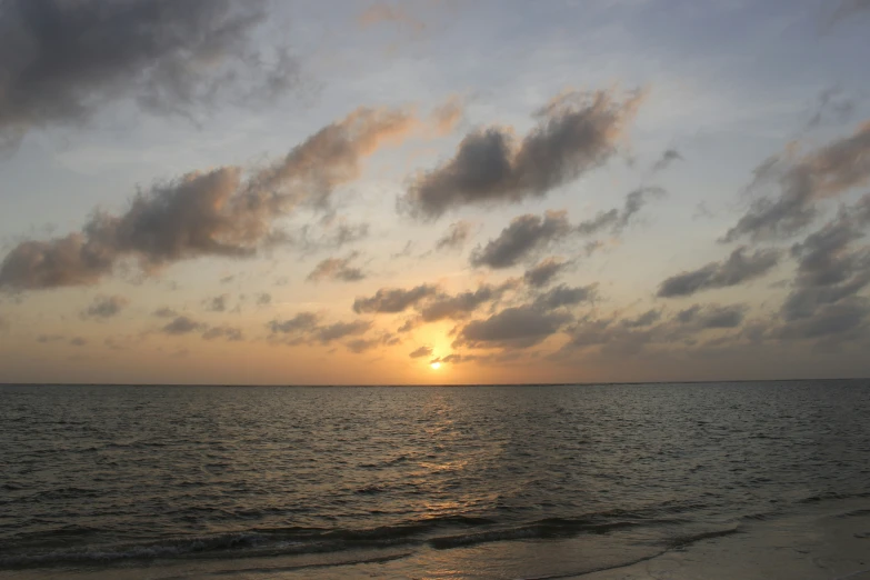 the sun sets over the water at a beach