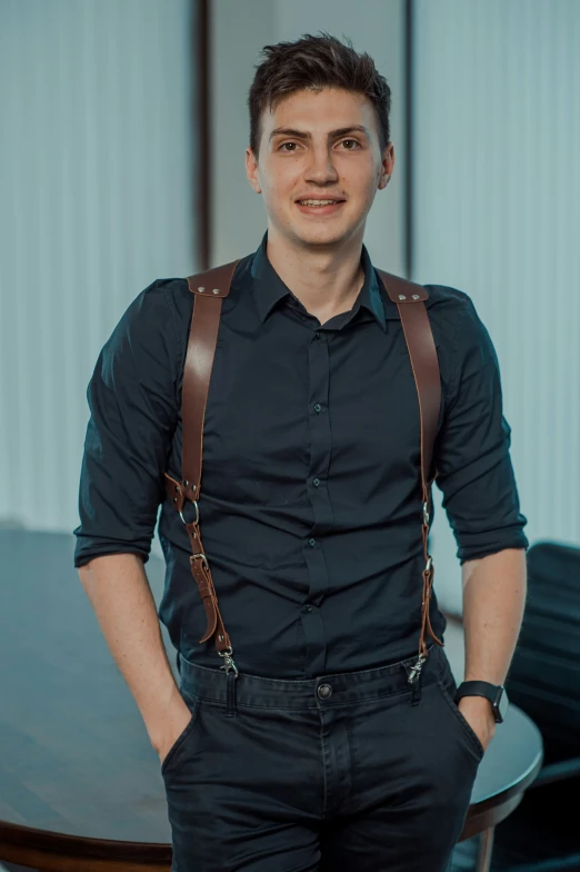 a man in black shirt and brown suspenders standing by a table