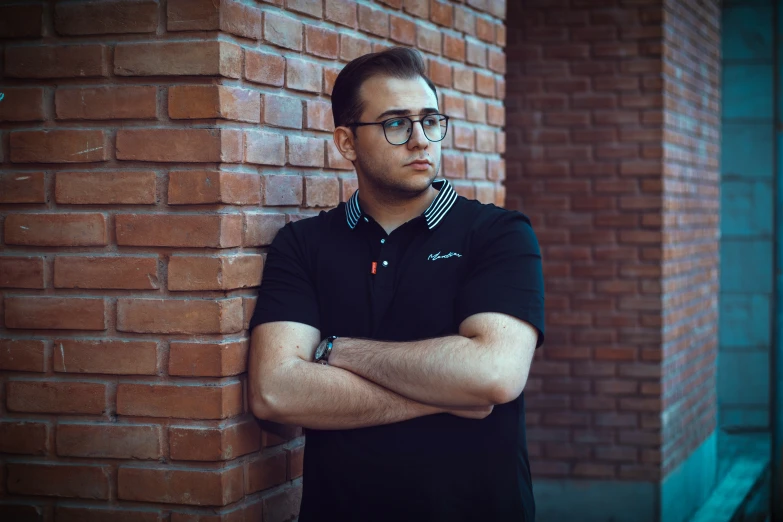 a man with his arms crossed by a brick wall