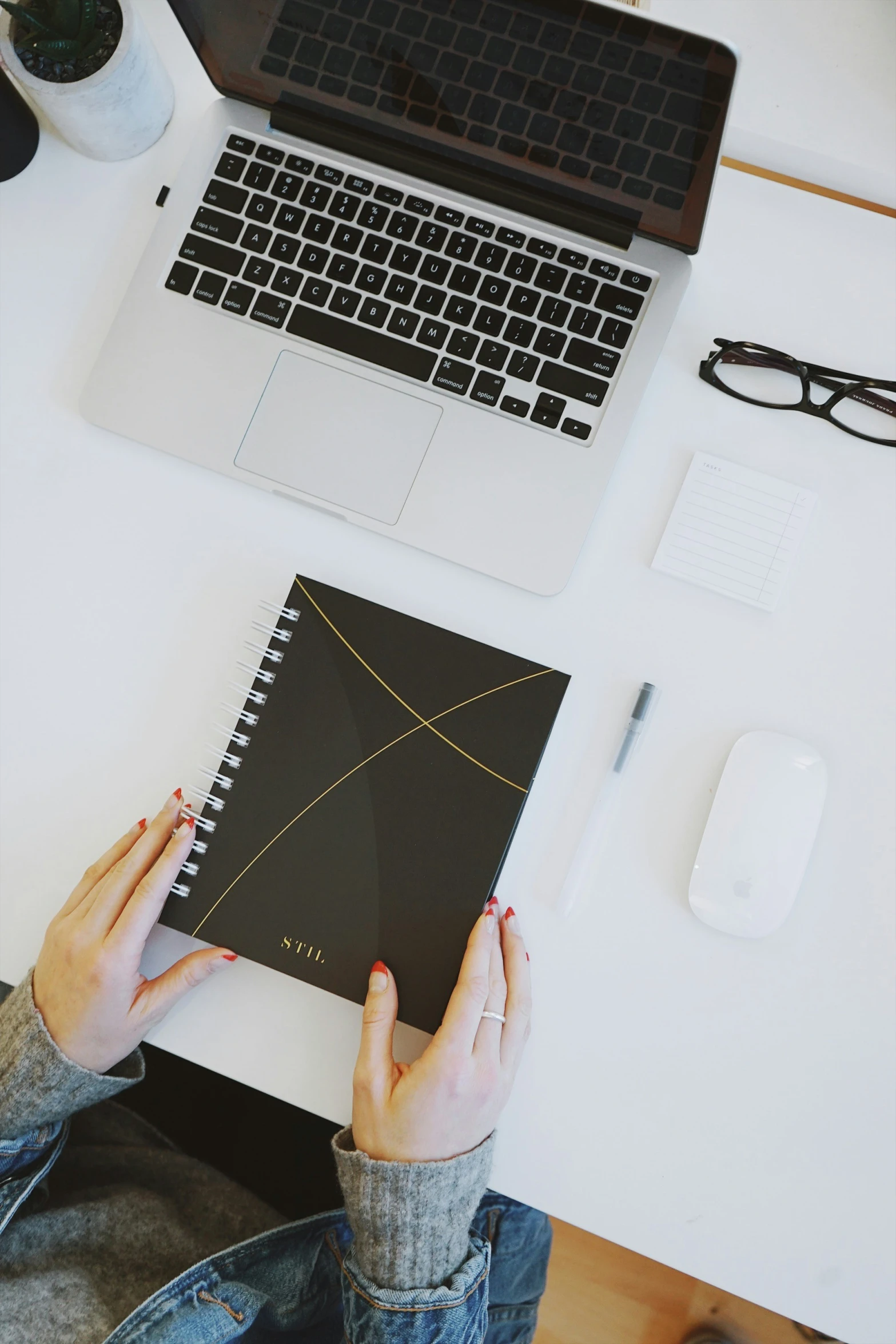 the person has notebook and a laptop on their desk