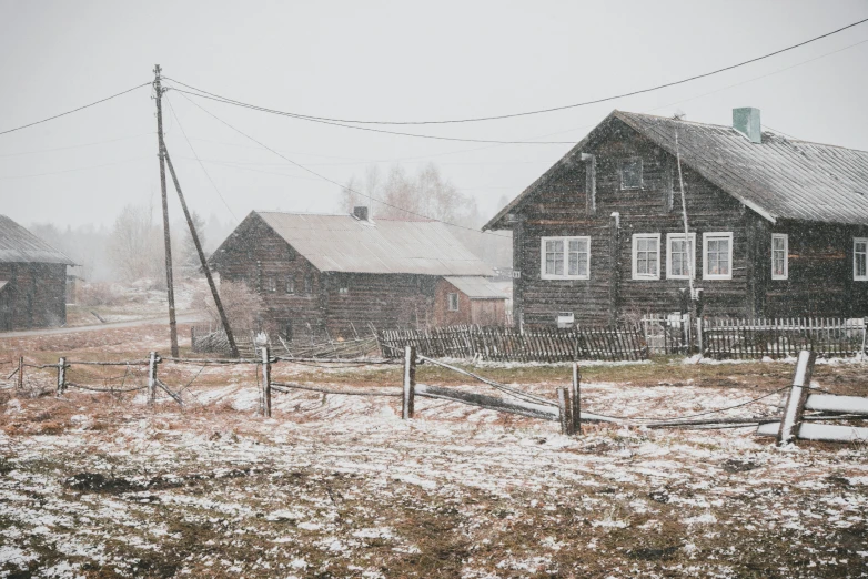 a house surrounded by snow and fence, with a field behind it