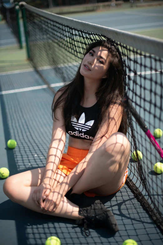 a woman sitting on the tennis court by some tennis balls