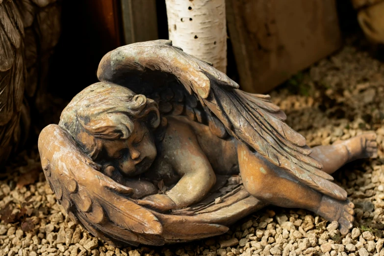 small statue with wings sitting on gravel next to a white birch