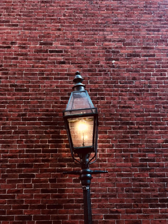 an old fashioned street lamp near a brick wall