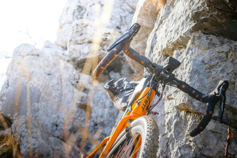 an orange bike against a stone wall and rocks