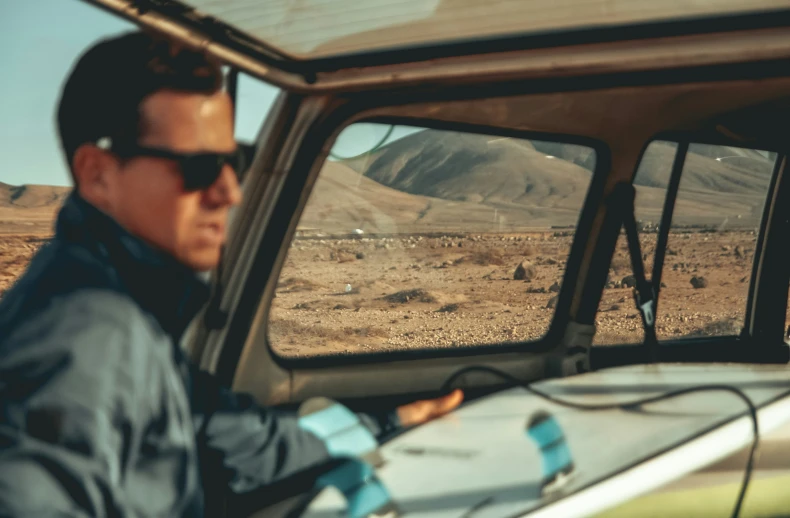 a man drives through desert with mountains in the background