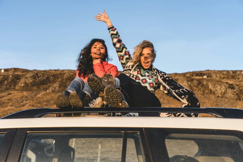 two women are sitting on the roof of a car