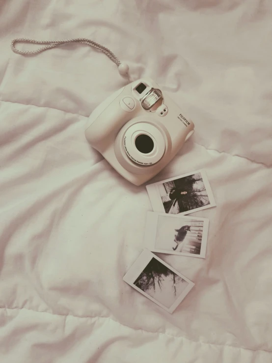 a camera laying on top of a white bed next to three pictures