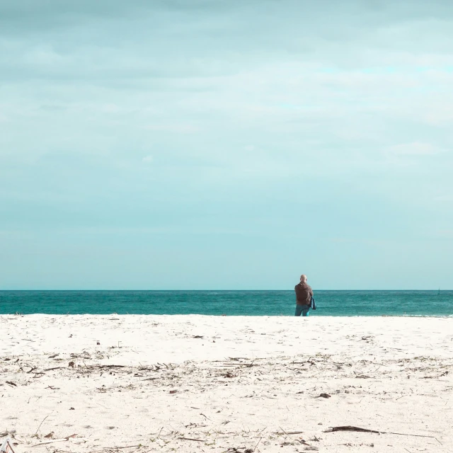 a person is standing in the sand looking at a large body of water