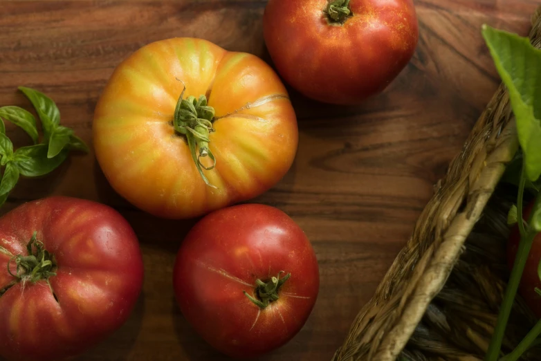 four tomatoes and one basil sit on a wooden table