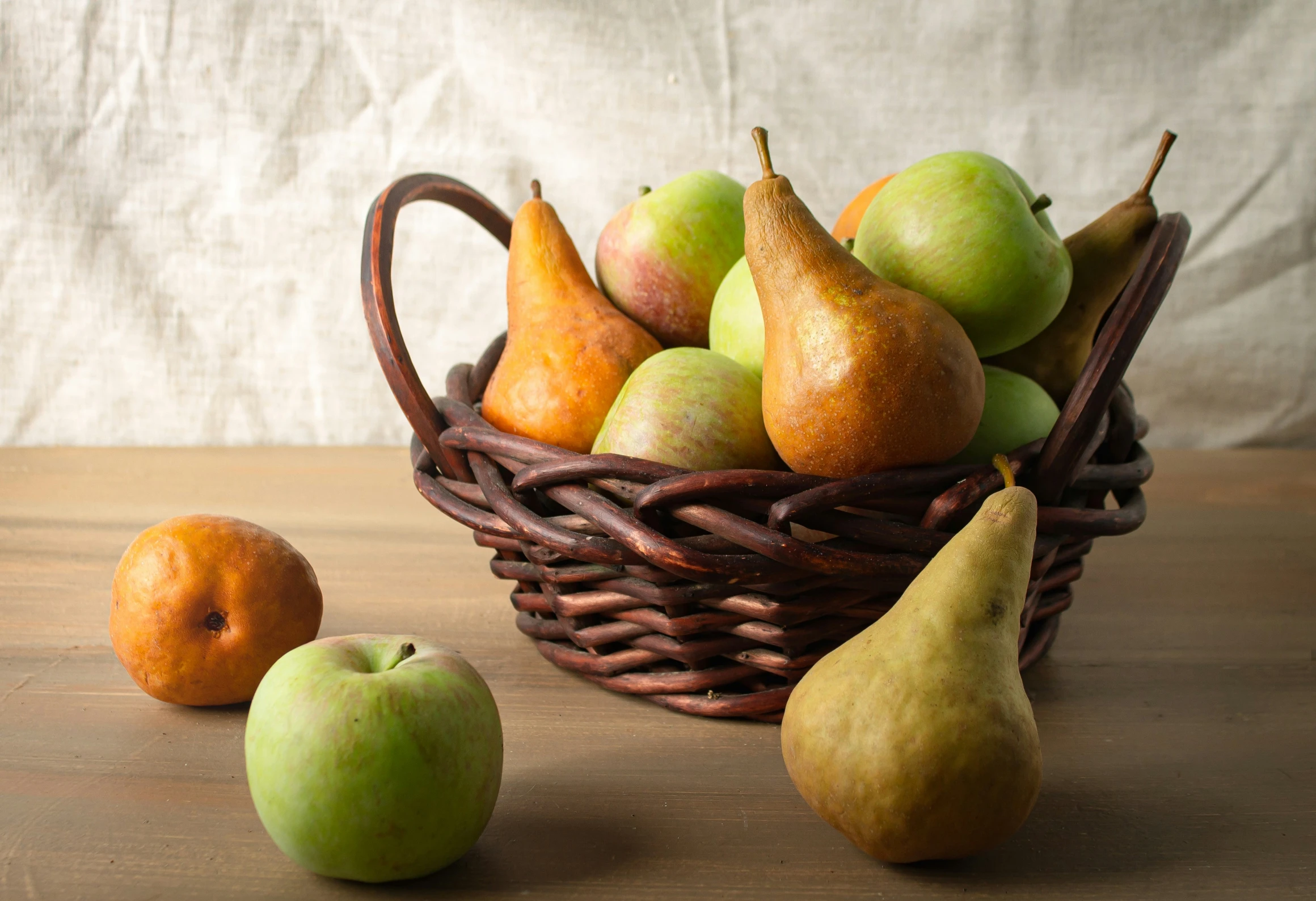 a wicker basket of pears, apples, and oranges on a wooden table