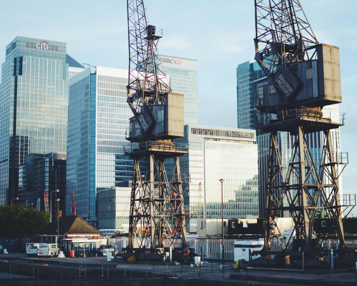 some construction cranes and a clock near other city buildings