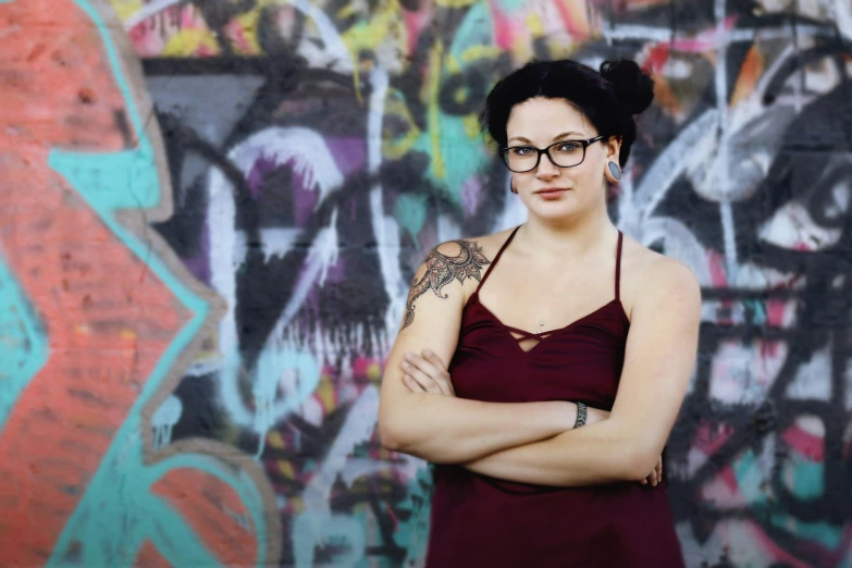 a woman in glasses with her arms crossed next to a wall