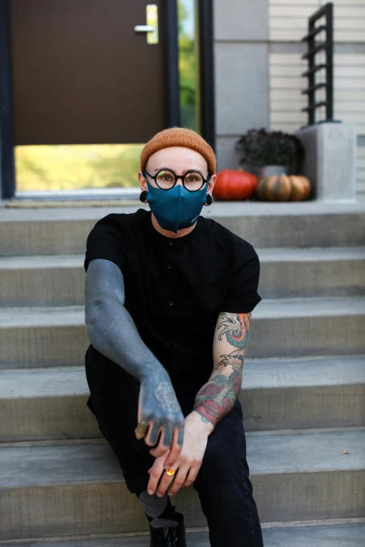 a person in black is sitting down wearing a face mask and black boots