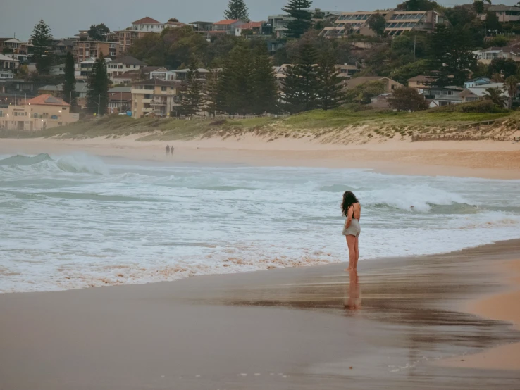 a woman in white bikini standing at the ocean's edge