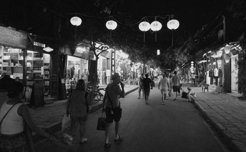 a dark street with hanging lights and people on it