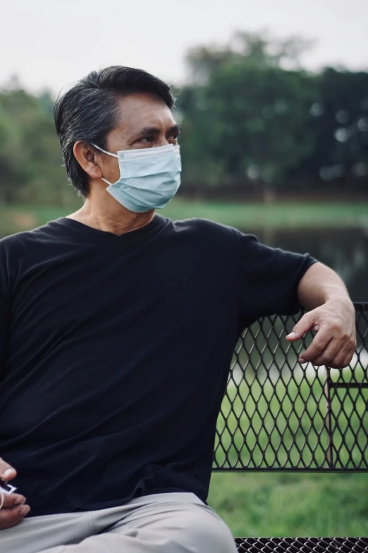 a man wearing a surgical mask sitting on a bench