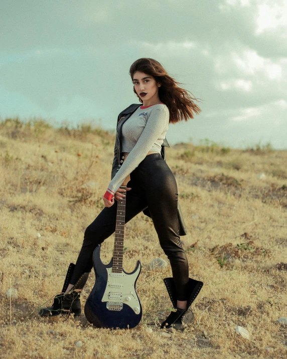 young woman standing with a guitar outdoors in a field