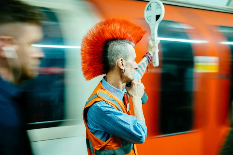 man in an orange mohawk on train talking on a phone