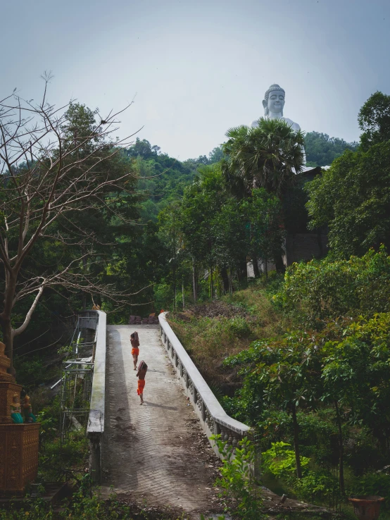 three children are walking across a bridge that runs above a lush green hillside