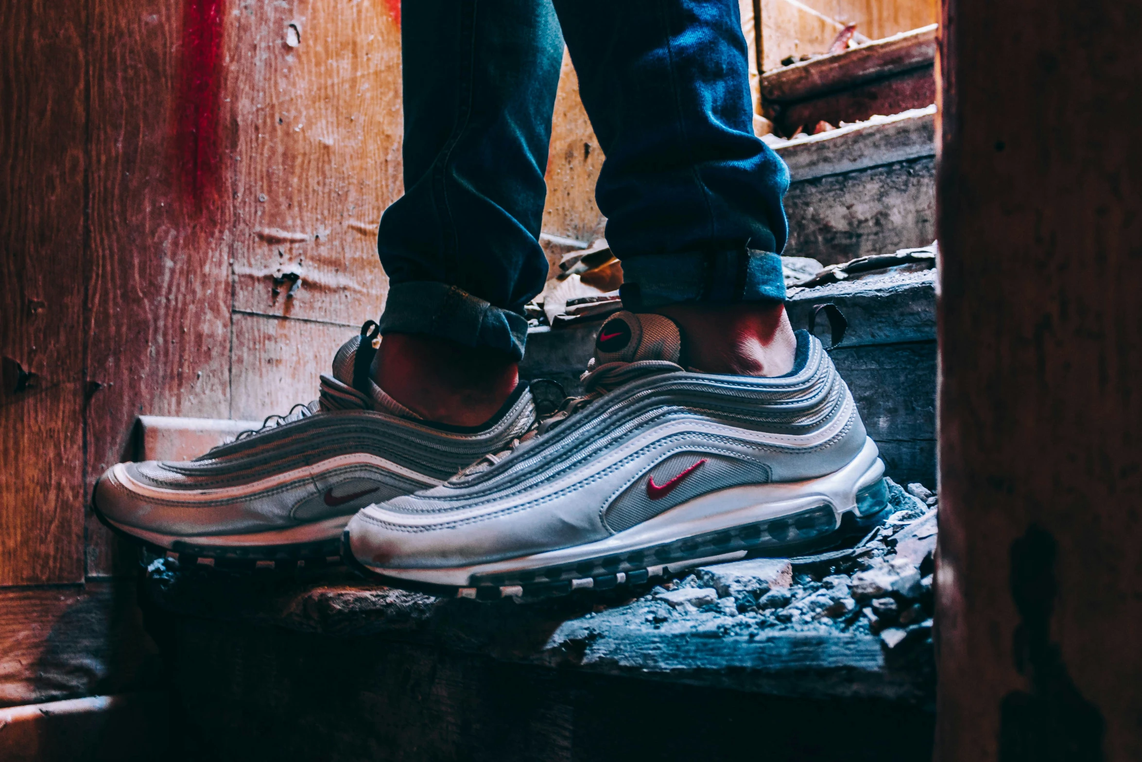 a pair of legs standing on a ledge, while wearing nike air max 97 shoes