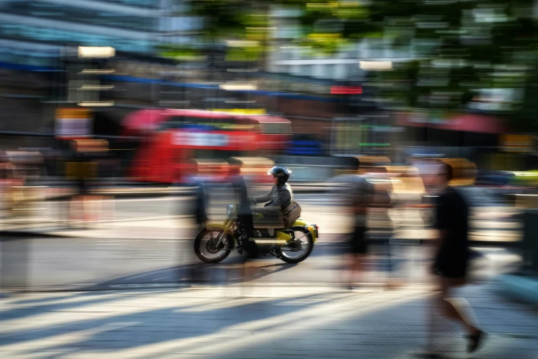 the blurry po shows people walking by, the person on the motorcycle is riding down the street