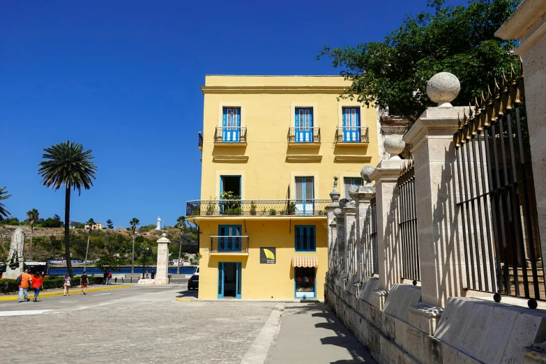 a large yellow building has blue windows and a wrought iron fence