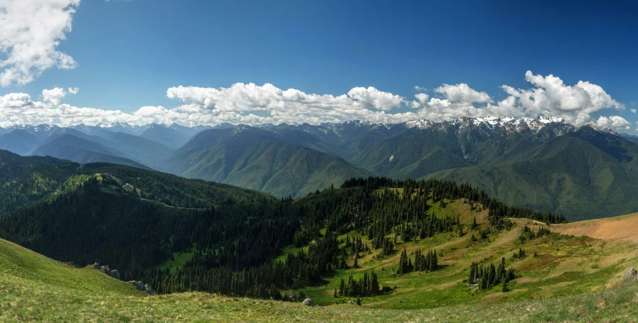 the mountains are covered with trees as clouds hover overhead