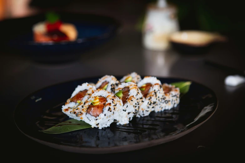 a black plate topped with sushi next to another plate filled with food