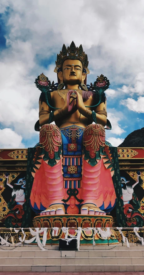 a statue of a person sitting on the ground with mountains behind it