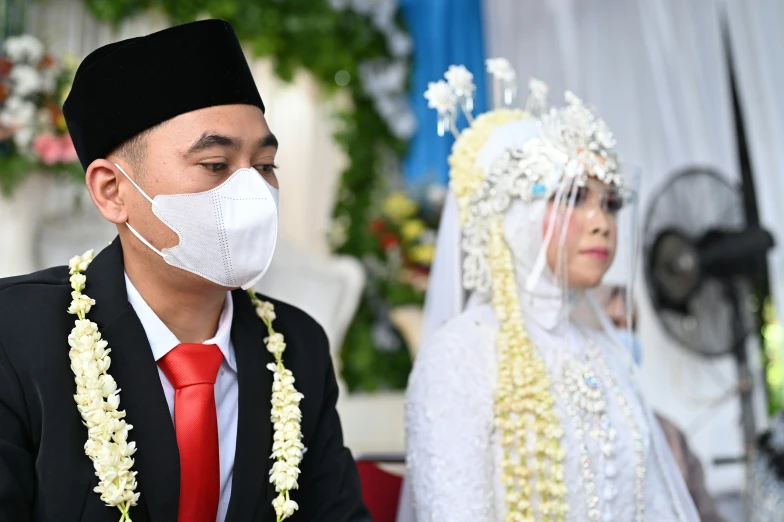 an asian bride and groom with a mask covering their face