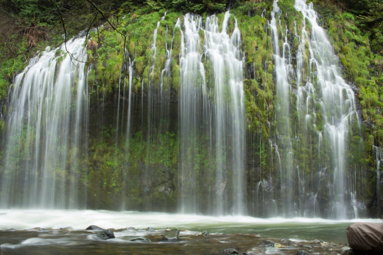 a person kneeling down looking at a tall waterfall