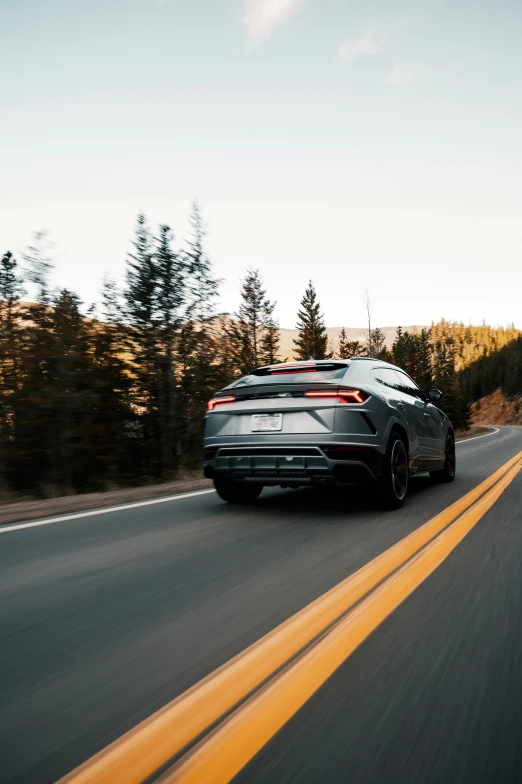 a grey car is driving down the road with trees