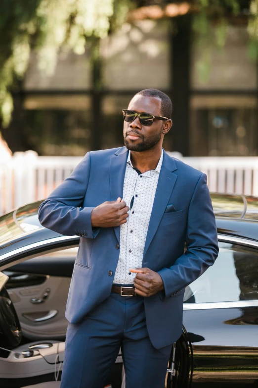 a black man in sunglasses standing next to his car