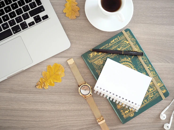 a laptop and a desk with coffee, pencils, a watch and papers