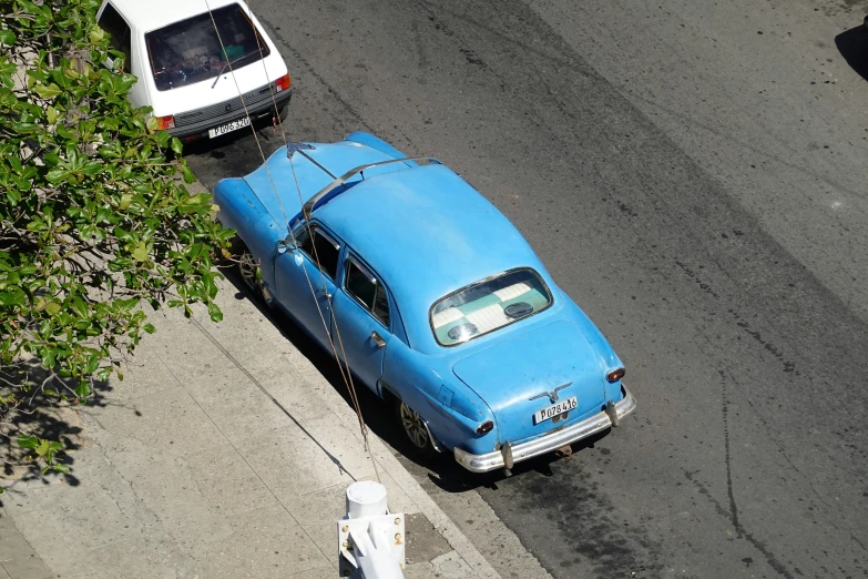 an old blue car driving down the street