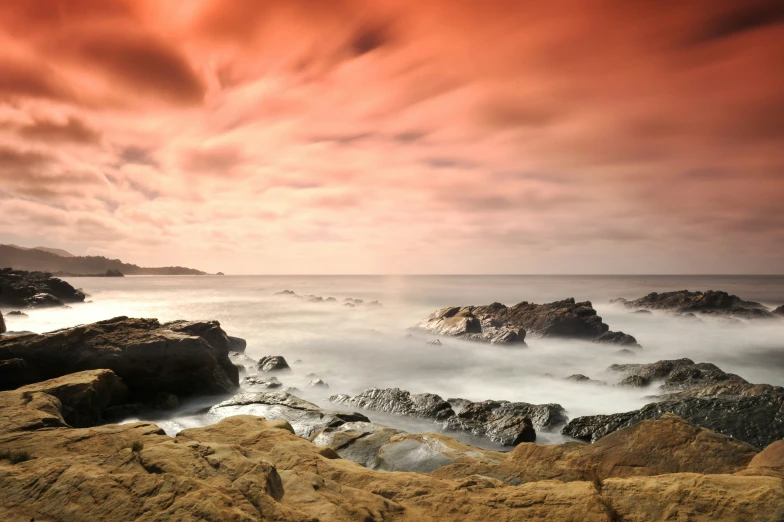 rocks and ocean under a red sky and white clouds