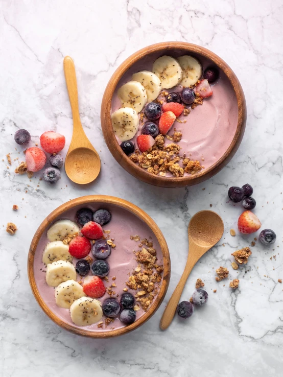 two bowls of yogurt and fresh fruit on a marble surface