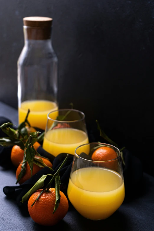 a group of glasses filled with orange juice next to oranges