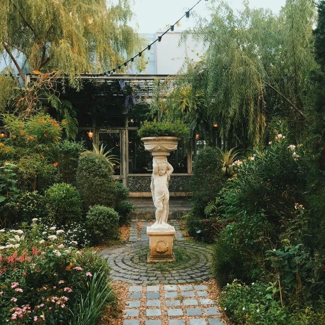 a stone statue surrounded by flowers and shrubbery